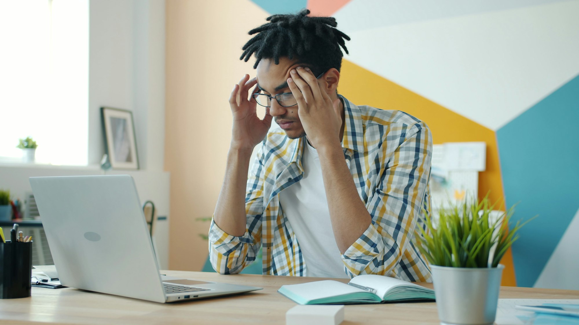 A developer sitting at a desk with a laptop, head in hands